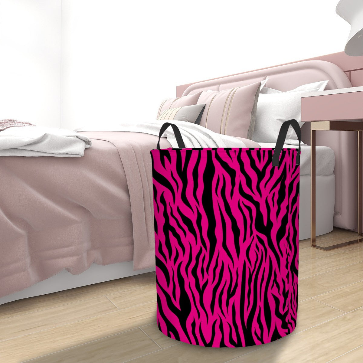 Pink and black tiger stripe animal print pattern laundry basket on a wooden floor with a bed in the background.