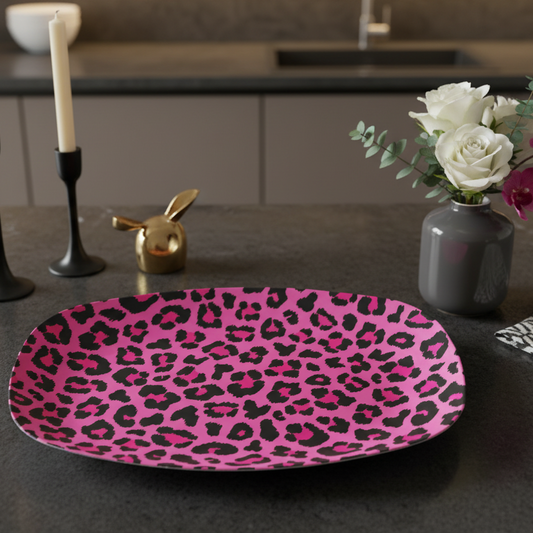 Pink leopard print platter on a dark surface with candles, flowers, and decor items.