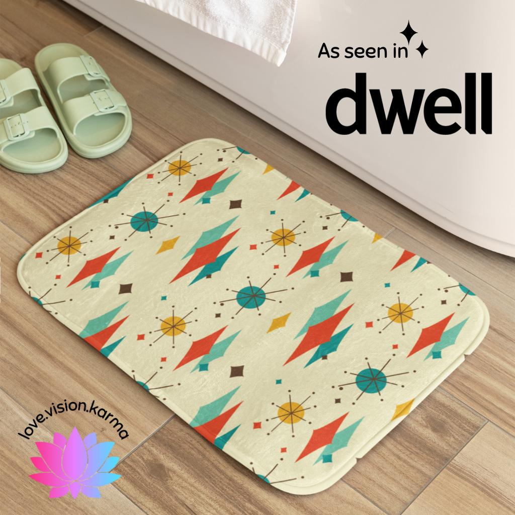 A vintage 1950's inspired bath mat with a geometric pattern featuring atomic diamonds and bursts, in retro shades of teal and orange, placed on a bathroom floor.